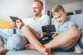 Father and son, PC gamers, enthusiastically playing with electronic devices: tablet and gamepad