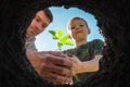 Father and son planting plant in soil together. Child farmer with strawberry seedlings lowers sprout into hole with ground