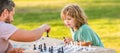 Father and son play chess outdoor, banner poster with copy space, strategic and tactic. tutorship. dad and kid play