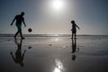 Father and son play soccer or football on the beach, silhouette on sunset. Dad and child having fun outdoors. Royalty Free Stock Photo