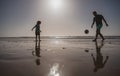 Father and son play soccer or football on the beach, silhouette on sunset. Dad and child having fun outdoors. Royalty Free Stock Photo