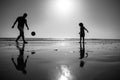 Father and son play soccer or football on the beach, silhouette on sunset. Dad and child having fun outdoors. Royalty Free Stock Photo