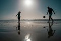 Father and son play soccer or football on the beach, silhouette on sunset. Dad and child having fun outdoors. Royalty Free Stock Photo