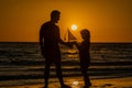 Father and son playing with toy sailboat, toy ship yacht on sea beach at summer sunrise. Sunset silhouette of father and Royalty Free Stock Photo
