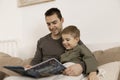 Father and son reading a book on the bed at home. Young attractive man and little boy resting in bedroom. Natural earth Royalty Free Stock Photo