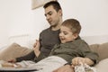 Father and son reading a book on the bed at home. Young attractive man and little boy resting in bedroom. Natural earth Royalty Free Stock Photo