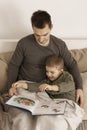 Father and son reading a book on the bed at home. Young attractive man and little boy resting in bedroom. Natural earth Royalty Free Stock Photo