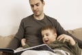 Father and son reading a book on the bed at home. Young attractive man and little boy resting in bedroom. Natural earth Royalty Free Stock Photo