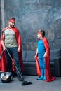 Father and son in red superhero costumes vacuuming carpet