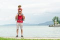 Father and son on shoulders stand on the pier on the sea background, lighthouse and mountains in the distance Royalty Free Stock Photo