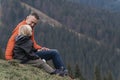 Father and son sit on hillside on the forest background. Weekend hike in mountains. Trekking and hiking with children