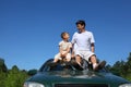 Father and son sit on roof of car in day