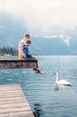 Father with son sit on the wooden pier and look on white swan sw Royalty Free Stock Photo