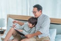 Father and son sitting on the bed doing homework writing on a book together, Father teaching son to write with smile Royalty Free Stock Photo