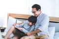 Father son sitting on the bed doing homework writing on a book together, Father teaching son to write with smile Royalty Free Stock Photo