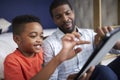 Father With Son Sitting In Bedroom Playing Game On Digital Tablet Together Royalty Free Stock Photo