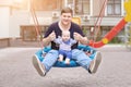 Father with son sitting on big modern chain swing and laughing. Parent with baby boy enjoying swinging on seesaw at playground. Ha