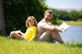 Father and son sitting on green grass in garden and reading book together. Happy family reading book together in green Royalty Free Stock Photo