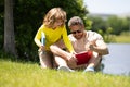 Father and son sitting on green grass in garden and reading book together. Happy family reading book together in green Royalty Free Stock Photo