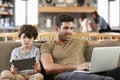 Father And Son Sitting On Lounge Sofa Using Digital Devices Royalty Free Stock Photo