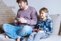 Father And Son Sitting On Sofa In Lounge Playing Video Game Royalty Free Stock Photo