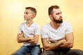 Father and son sitting together against yellow background. Quarrel, resentment, insult, offense concept