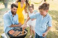 Father and son preparing meat on charcoal barbecue grill during picnic