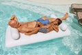 Father And Son Sunbathing In Pool. Little Boy With Dad Floating On Inflatable Water Mattress.