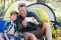 Father and son taking selfie by tent in forest Royalty Free Stock Photo