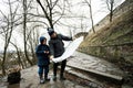 Father and son tourist look at map, stand on wet path to an ancient medieval castle fortress in rain