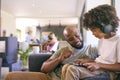 Father And Son Using Digital Tablet With Headphones At Home With Multi-Generation Family Behind Royalty Free Stock Photo