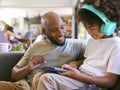 Father And Son Using Digital Tablet With Headphones At Home With Multi-Generation Family Behind Royalty Free Stock Photo