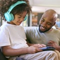 Father And Son Using Digital Tablet With Headphones At Home With Multi-Generation Family Behind Royalty Free Stock Photo