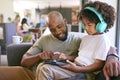 Father And Son Using Digital Tablet With Headphones At Home With Multi-Generation Family Behind Royalty Free Stock Photo