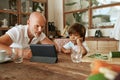 Father And Son Using Tablet At Kitchen Table. Dad And Kid Sitting At Home And Enjoying Leisure At Tropical Resort. Royalty Free Stock Photo