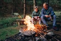 Father with son warm near campfire, drink tea and have conversation Royalty Free Stock Photo