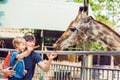 Father and son watching and feeding giraffe in zoo. Happy kid ha