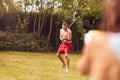 Father And Son Wearing Swimming Costumes Having Water Fight With Water Pistols In Summer Garden