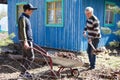 Father and son working together, gardener loading dried leaves in wheelbarrow from ground with shovel