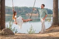 A father swings his daughter on a swing on the shore of a forest lake Royalty Free Stock Photo