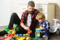 Father takes part in game with son playing on floor holding toy cars. Father and son create toys from bricks. Dad and Royalty Free Stock Photo