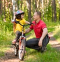 Father talking to his daughter, which teaches to ride a bike