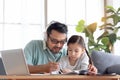 Father teaches cute girl daughter to do school homework, using laptop computer for e-learning study at home, happy family dad and Royalty Free Stock Photo