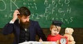 Father teaches son, discuss, explain. Teacher in formal wear and pupil in mortarboard in classroom, chalkboard on