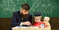 Father teaches son mathematics. Mathematics lesson concept. Teacher in formal wear and pupil in mortarboard in classroom Royalty Free Stock Photo