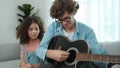 Father teaching daughter about playing guitar while sitting on sofa. Pedagogy. Royalty Free Stock Photo