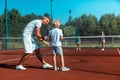 Father teaching his cute curly son to play tennis with family Royalty Free Stock Photo