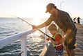 Father teaching little young son to be a fisherman, fishing together on sea dock embankment enjoying and learning using the fish r Royalty Free Stock Photo