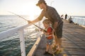 Father teaching little young son to be a fisherman, fishing together on sea dock embankment enjoying and learning using the fish r Royalty Free Stock Photo