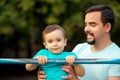 Father teaching toddler son to do pull ups exercise on steel bar outdoors. Healthy family, parental support and sports for kids
